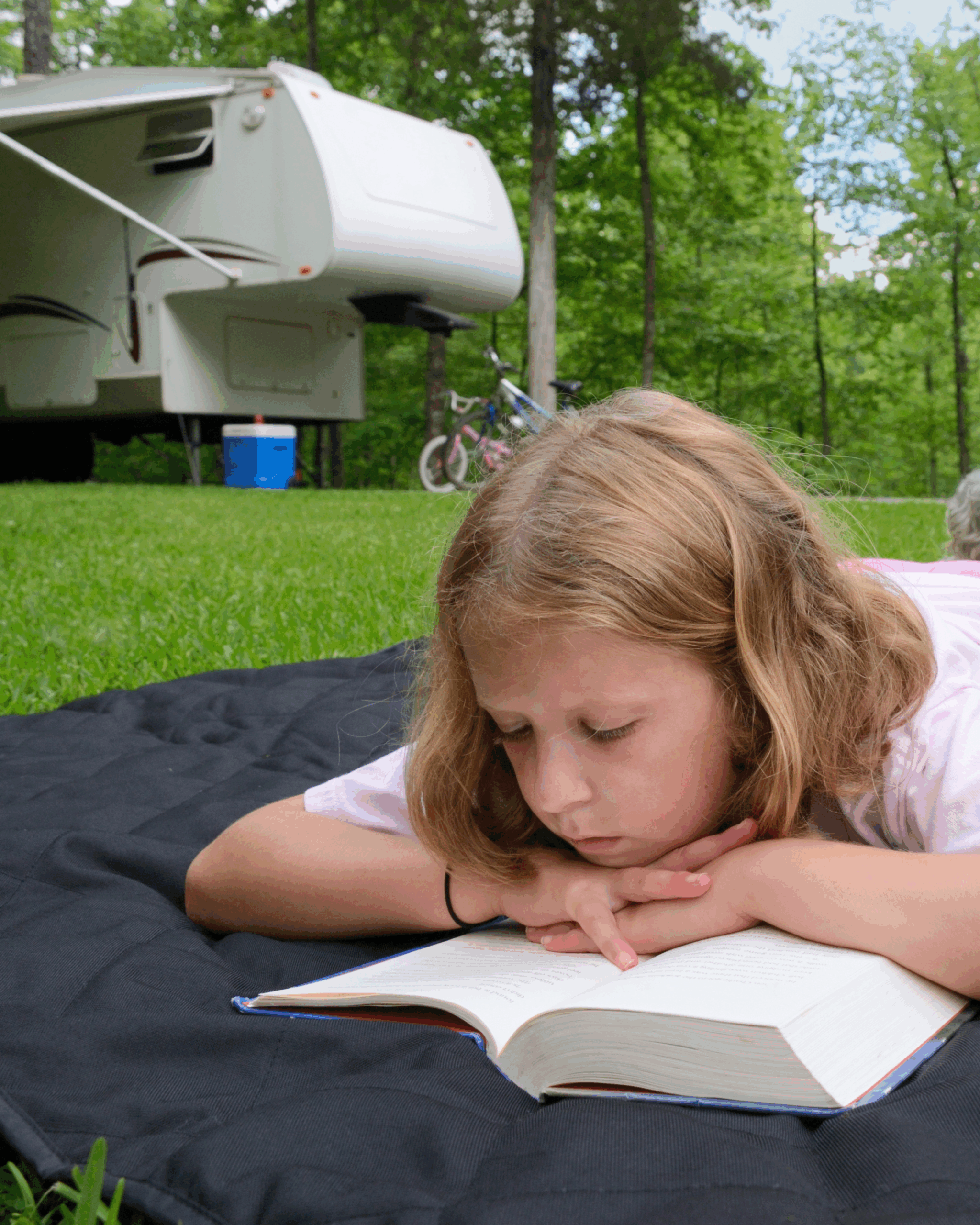 Girl reading a book outside her RV at a shaded, full-hookup campsite, similar to those at Legacy RV Resort in Darien, GA, in beautiful Coastal Georgia.